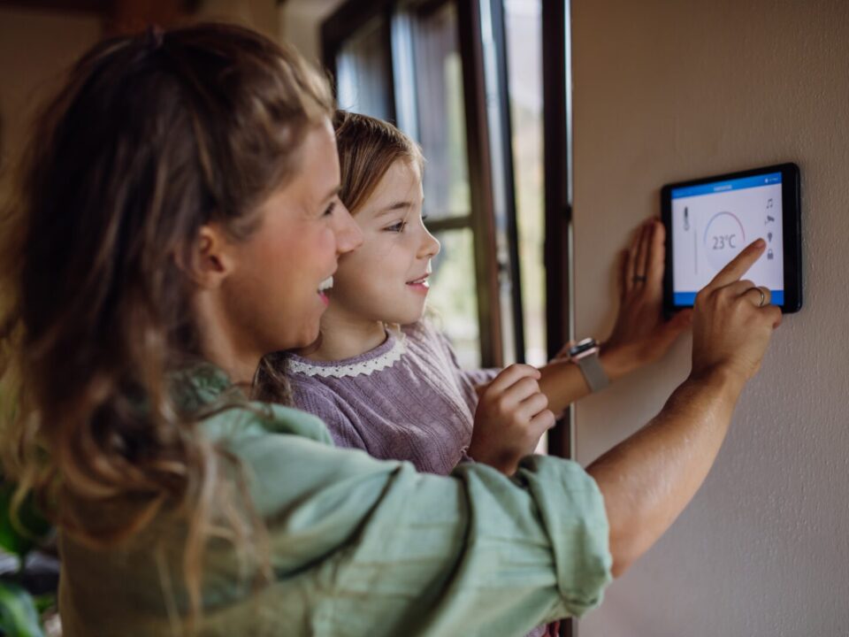 Girl,Helping,Mother,To,Adjust,,Lower,Heating,Temperature,On,Thermostat.